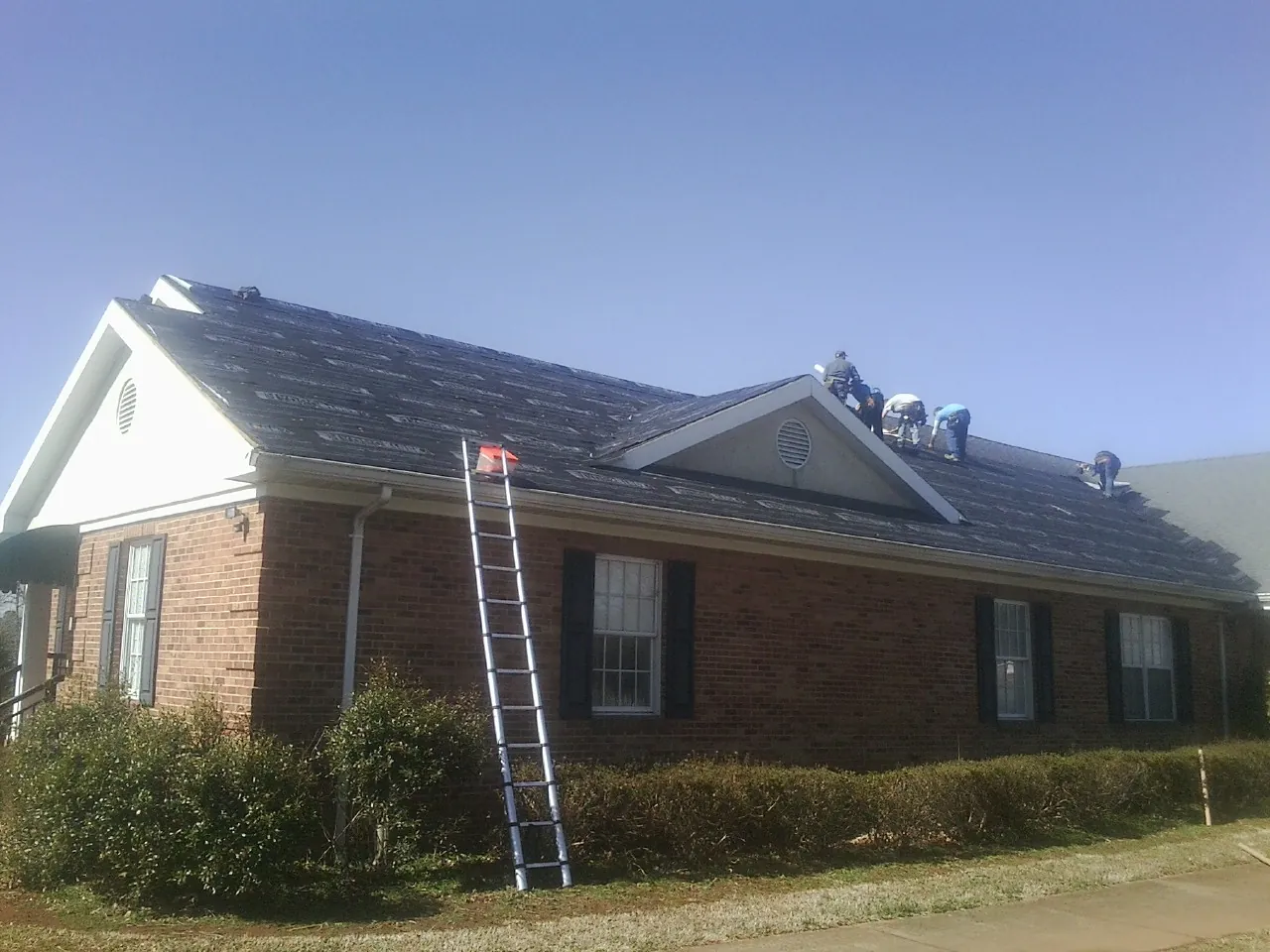 Crew tearing shingles off a brick ranch roof with a ladder set — Metal Roof Repair work by our crew in Pilot Hill