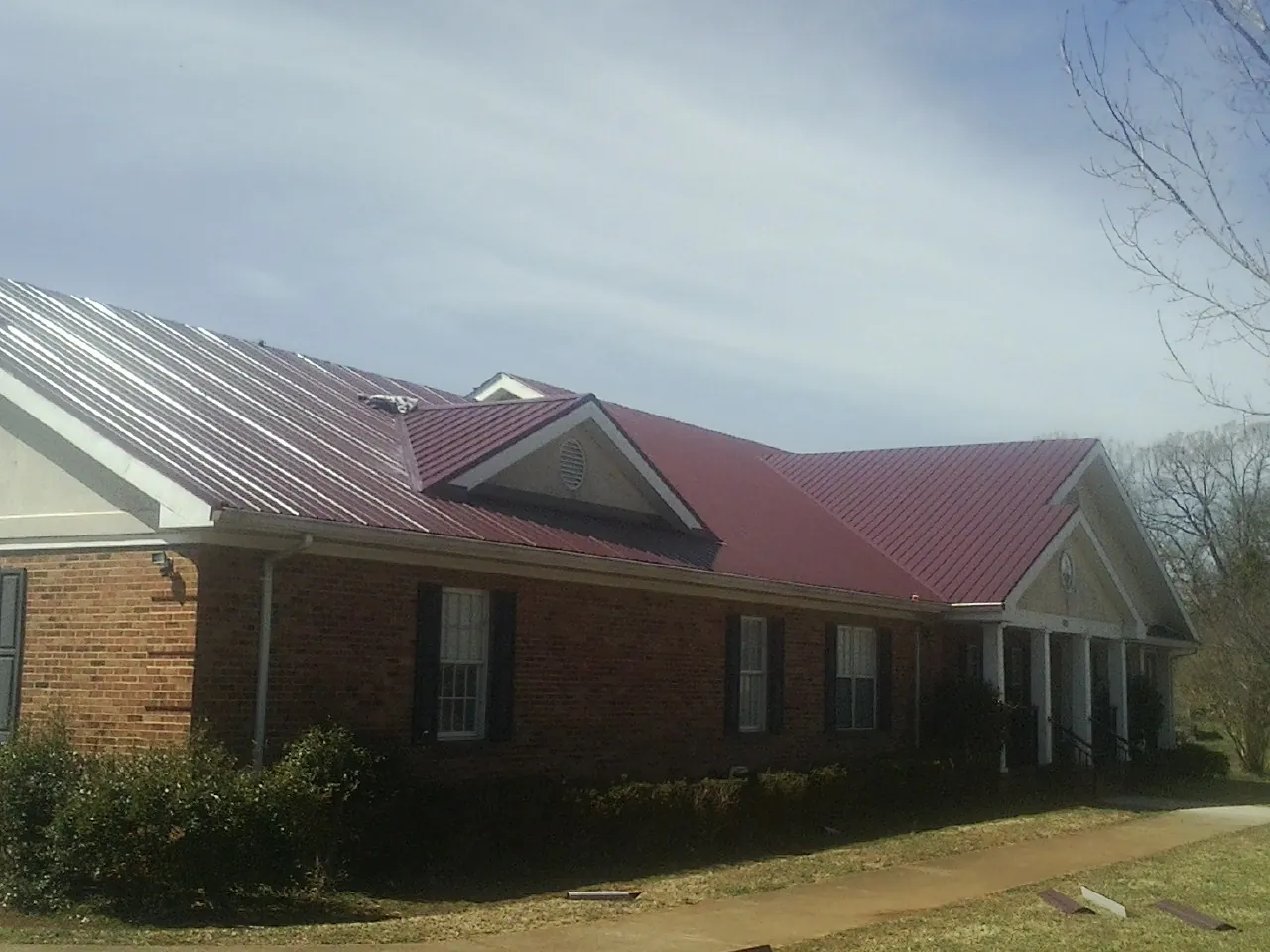 Red metal roof with gabled entries on a long brick building, from a Hail Damage Roof Repair job in Pilot Hill