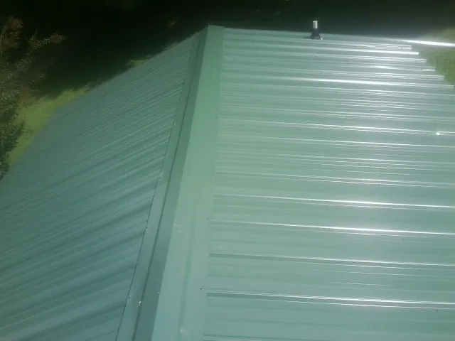New green metal panels meeting at the ridge of a roof — Flat Roof Repair work by our crew in Pilot Hill