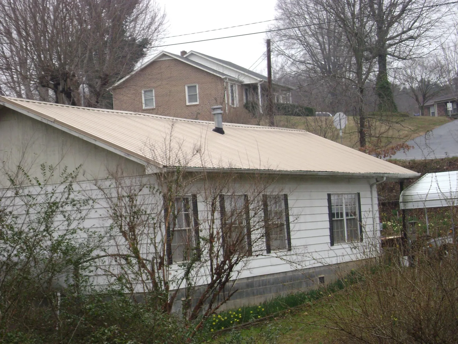 Tan metal roof on a white sided house set into a hillside — Commercial Roofing by Roofing Brothers in Pilot Hill
